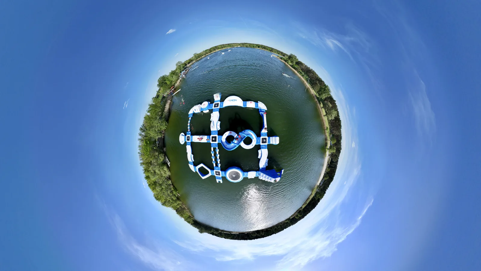 Der Aquapark am Bernsteinsee in Velten von oben: alle 28 Module als zusammenh&auml;ngender Parcours mitten auf dem See, ringsum Ufer und B&auml;ume.